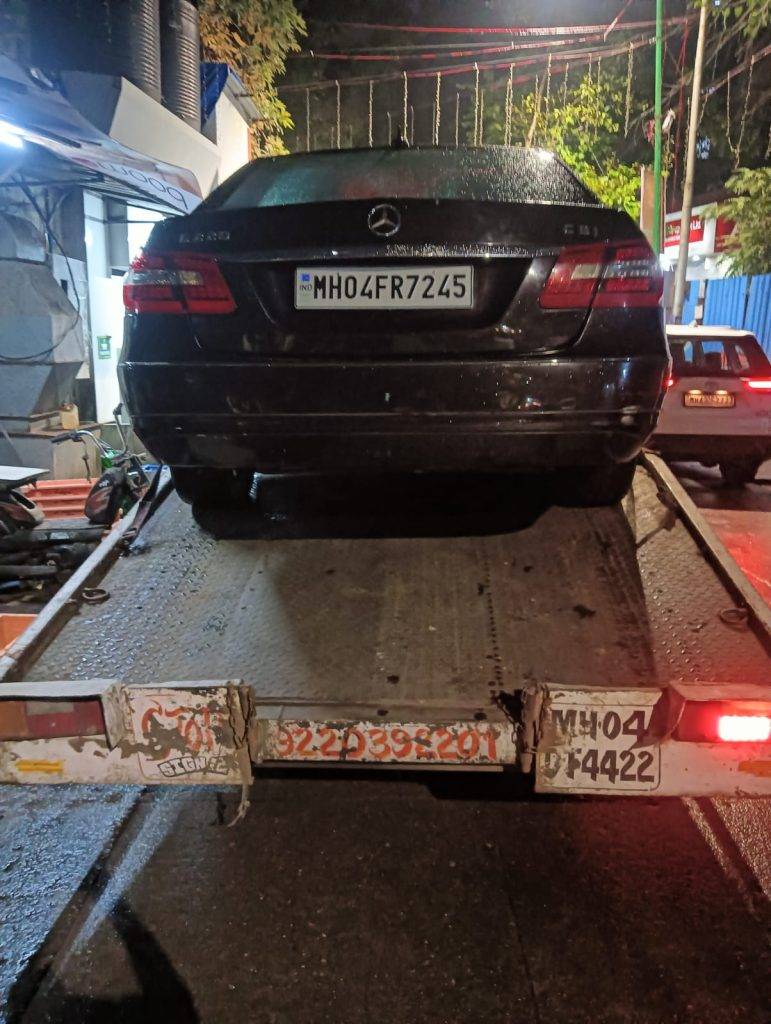 Dark Mercedes-Benz E-Class loaded onto a flatbed tow truck late at night in an urban area.