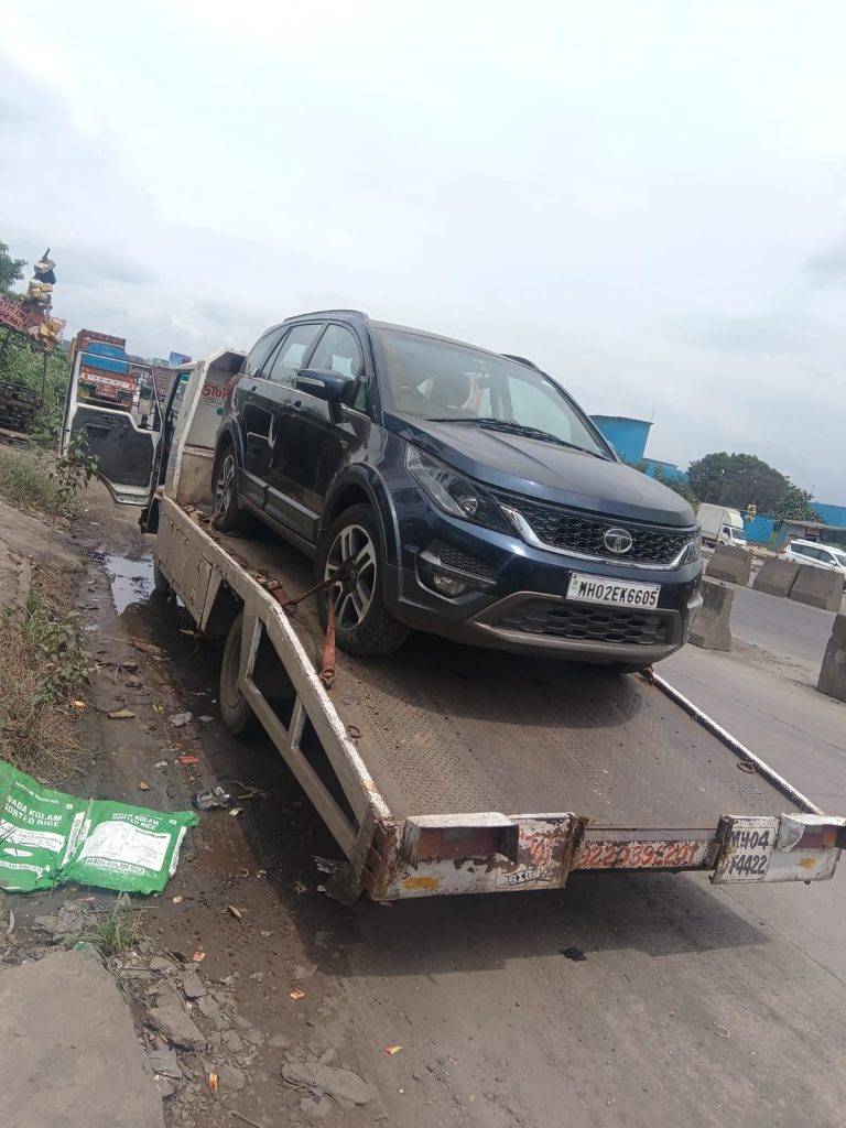 A dark blue Tata Hexa SUV being recovered and transported on a flatbed on the side of a highway.