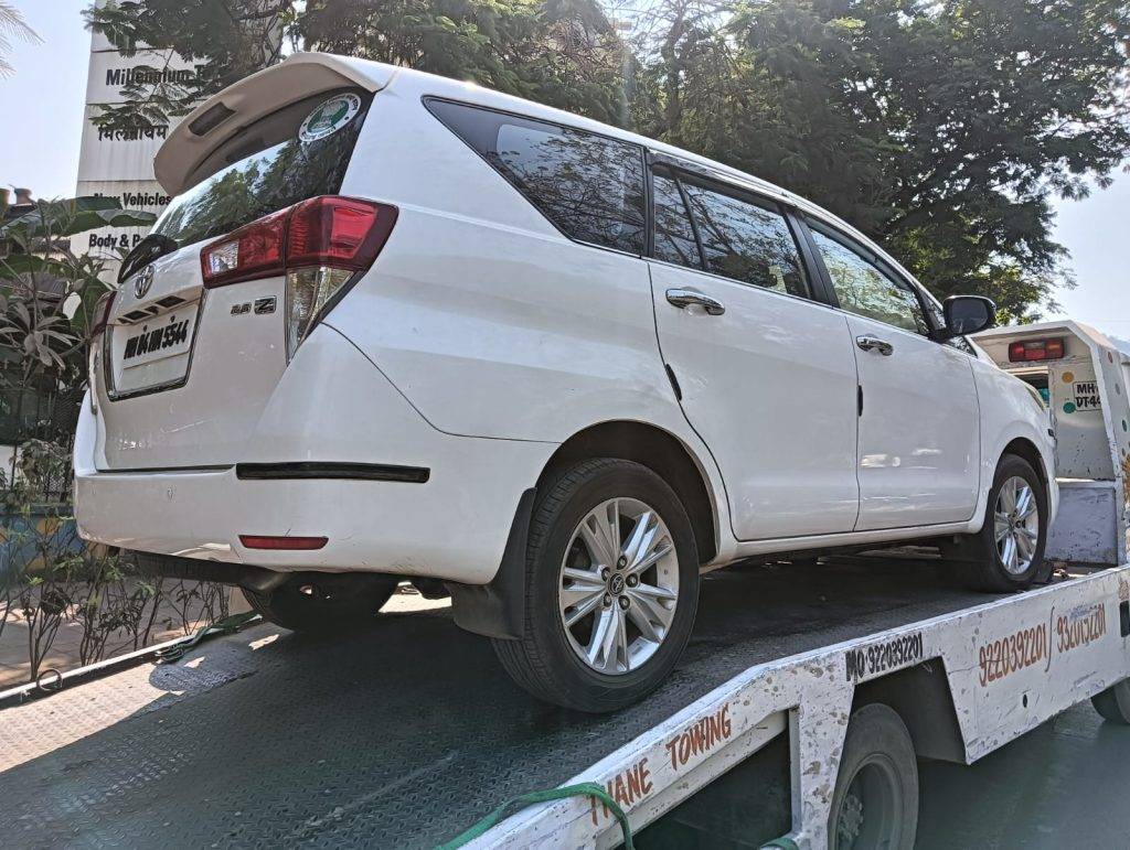 White Toyota Innova MPV loaded onto a flatbed tow truck with the 'Thane Towing' branding visible.