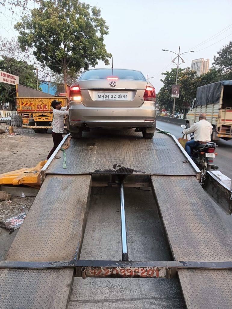 A gold Volkswagen Vento being loaded onto the flatbed tow truck with the hydraulic ramp fully extended.